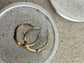 Handmade Home Accessories - A close up image of a white coaster with black splatters on holding a pair of gold hoops