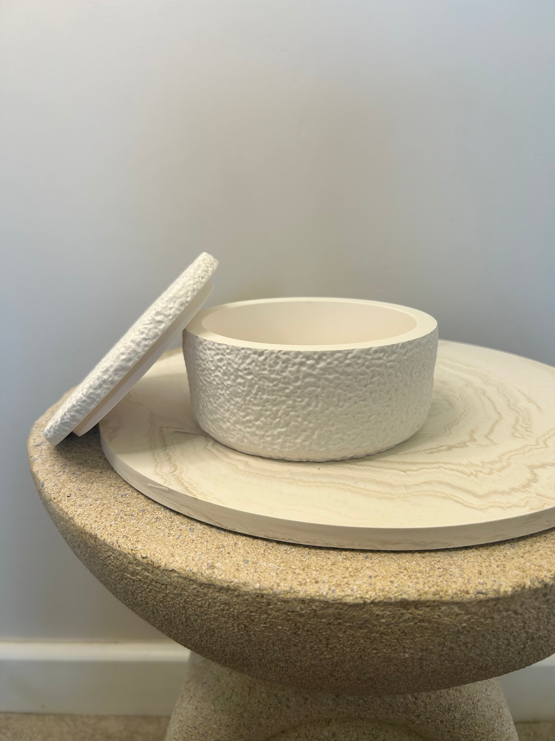 Handmade Home Accessories - a shot front on of the griege marble display plate with an open teddy texture pot on a natural stone table.