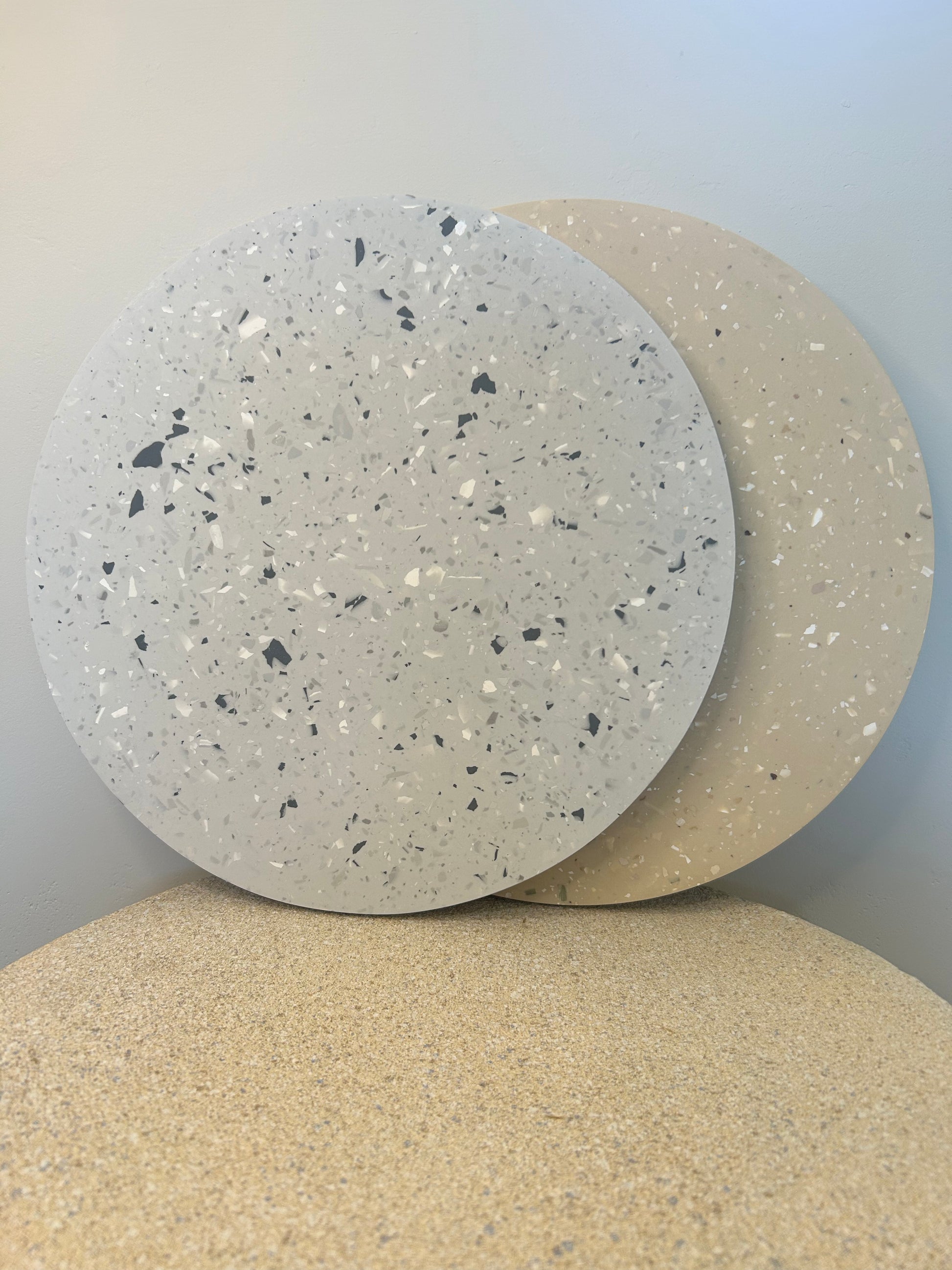 Handmade Home Accessories - a front on view of two terrazzo style trays, one beige and one gray on a stone textures table against a griege wall