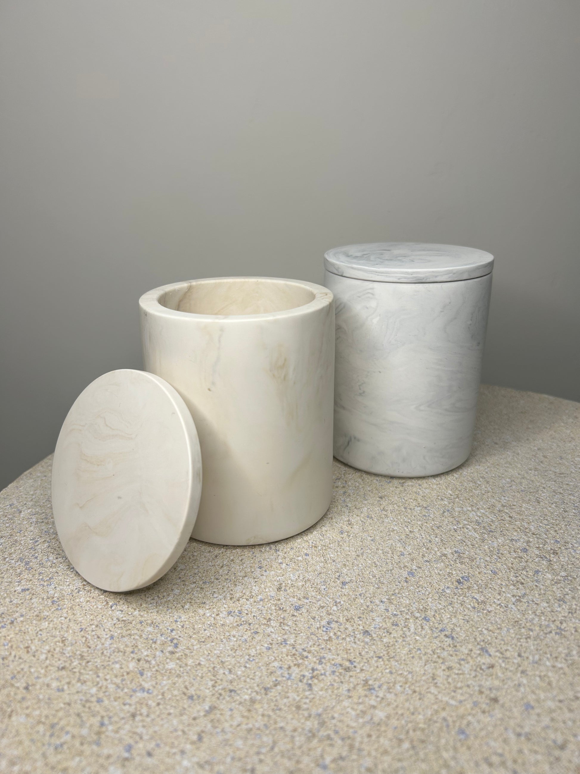 Handmade Home Accessories - two marble pots one grey and one beige against a neutral background, one  has a lid on, one does notr