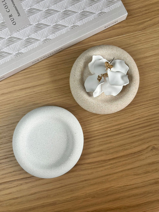 Pair of round speckled Jesmonite trays, one styled with sculptural white floral earrings. Elegant handmade home accessories perfect for bedside or dressing tables.