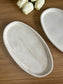 Handmade oval trinket dish in a marbled cream finish with organic swirls, styled with white tulips on a wooden surface, ideal for home accessories.
