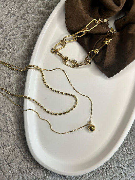 White oval ceramic dish styled with layered gold necklaces and a brown scrunchie, set on a grey textured fabric background, perfect for elegant home storage.