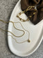White oval ceramic dish styled with layered gold necklaces and a brown scrunchie, set on a grey textured fabric background, perfect for elegant home storage.