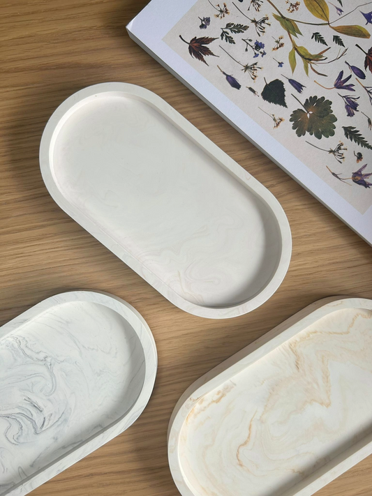 Flat lay of three oval handmade Jesmonite trays in soft marble finishes, styled with a pressed flower book – perfect as sustainable, minimalist home accessories.