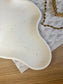 Close-up of organic-shaped white Jesmonite tray with subtle black speckle pattern, styled beside gold chain jewellery – modern handmade home accessory.