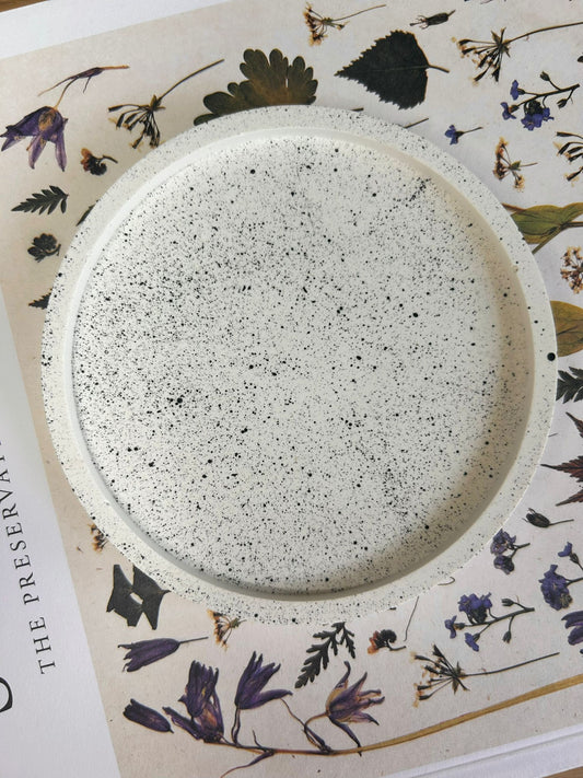 Round handmade Jesmonite coaster with black splatter design on white base, styled on a floral print background – artistic and modern home accessory.