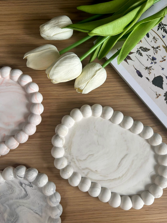 Flat lay of pebble-edged handmade Jesmonite trays styled with white tulips. Each tray features a unique marbled finish – a refined, eco-friendly home accessory.