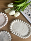 Flat lay of pebble-edged handmade Jesmonite trays styled with white tulips. Each tray features a unique marbled finish – a refined, eco-friendly home accessory.