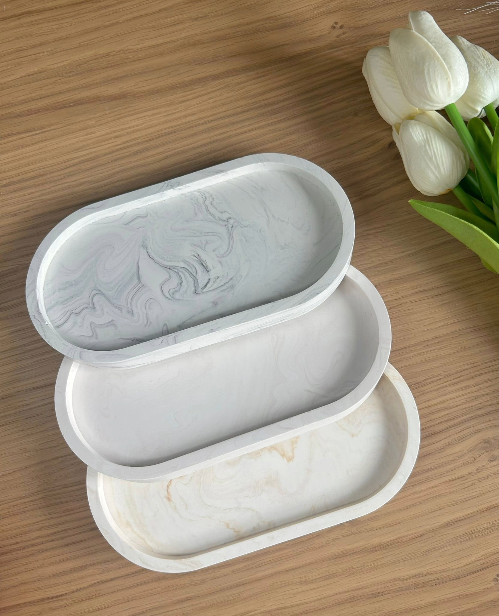 Handmade Jesmonite trays in grey, white, and beige marbling, arranged with white tulips. Stylish, eco-conscious home accessories for jewellery or keys.