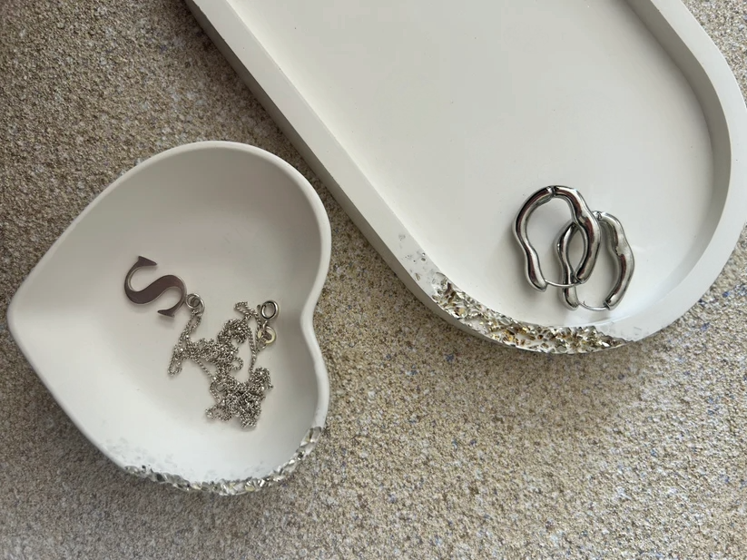 up shot of a white trinket tray and white heart trinket dish, showcasing a raw silver druzy style edge, with silvers hoops and a silver s necklace to accessorise.