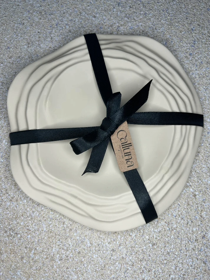 Handmade Home Accessories - Beige ripple trinket tray, with a black bow tied around with a tag that says Calluna Collection. the photo is taken to show off the packaging.