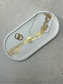 Handmade Home Accessories - Large Oval Trinket tray on a natural stone background, with cream main bod, that has black splatters and gold leaf detail. The picture is a 45 degree angle and the tray has a pair of gold hoop earrings and a star style coin necklace on for decorative purposes.