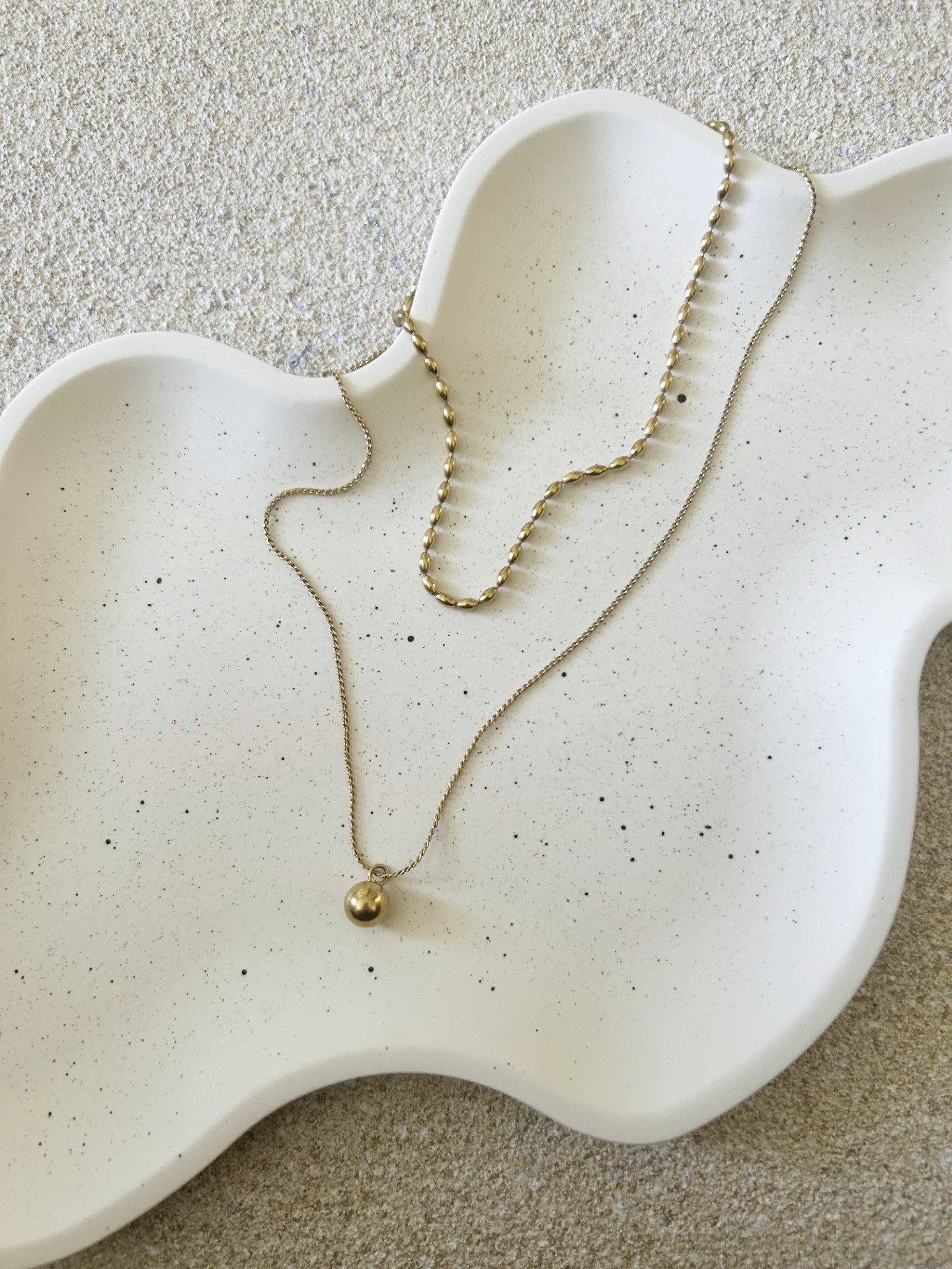 Handmade Home Accessories - close up shot of a wavy tray in white with black splatter pattern and a two tier gold necklace on it