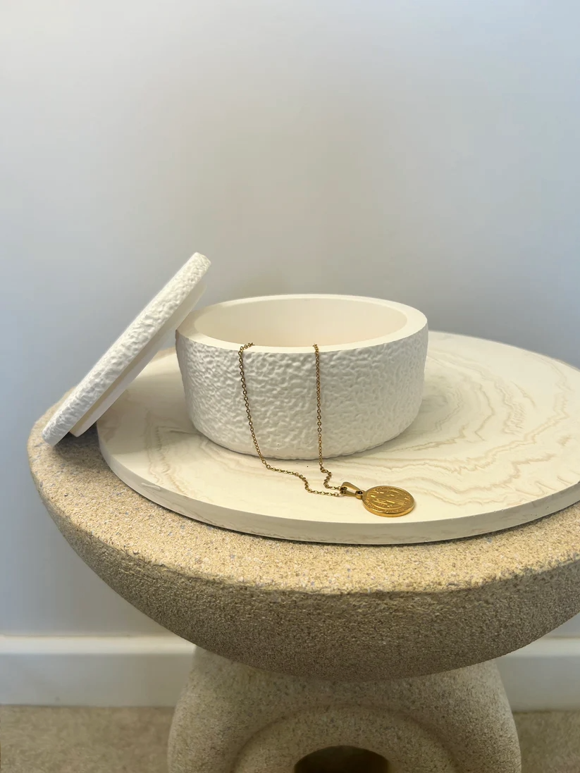 Handmade Home Accessories - a white textured pot, with the lid resting against the side and a gold coin necklace draping over the edge