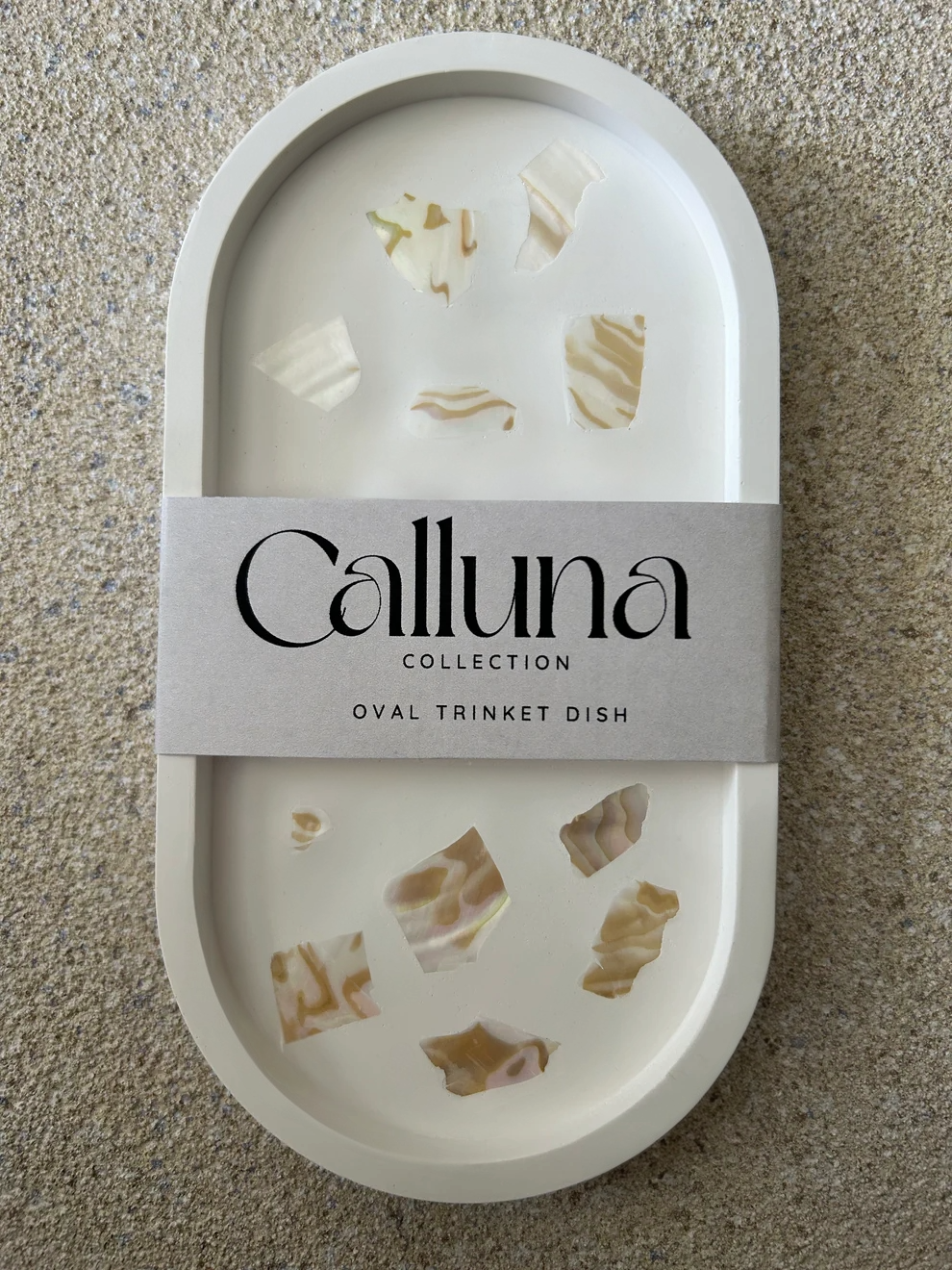 Handmade Home Accessories - A vertical shot of an oval trinet tray in white that has cream abalone shell details and a belly band around the centre with the company name Calluna Collection on.