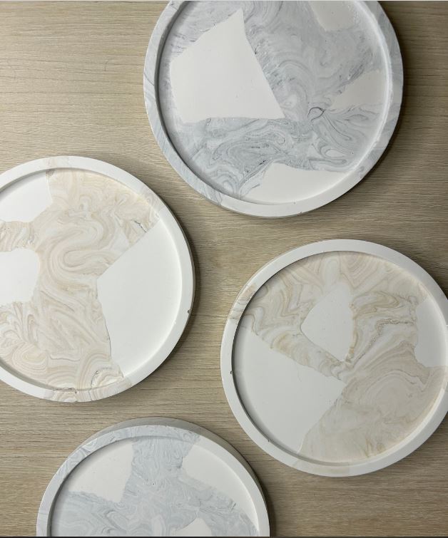 Handmade home Accesories - a birds eye view shot of 4 coasters some beige marble and white and some grey marble and white, spread on a table made of light wood.