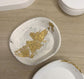 Handmade Home Accessories - An oval small trinket dish in cream, with black splatters and gold leaf details on a light wood surface.