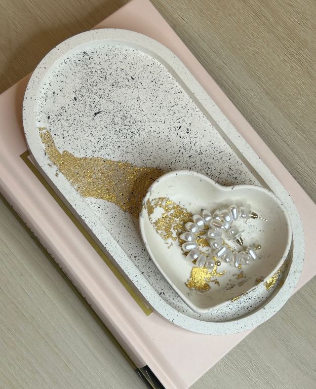 Handmade Home Accessories - A oval shaped trinket tray in cream, with black splatters and gold leaf details with a matching heart small dish with pearl earrings in, perched on some books for decorative purposes.