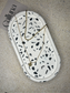 Handmade Home Accessories - A full length shot of a oval shaped trinket tray that is made using black obsidian gemstones to create terrazzo effect and give a monochrome look. it is on a natural stone backdrop and has a two tiered gold necklace on for display purposes.