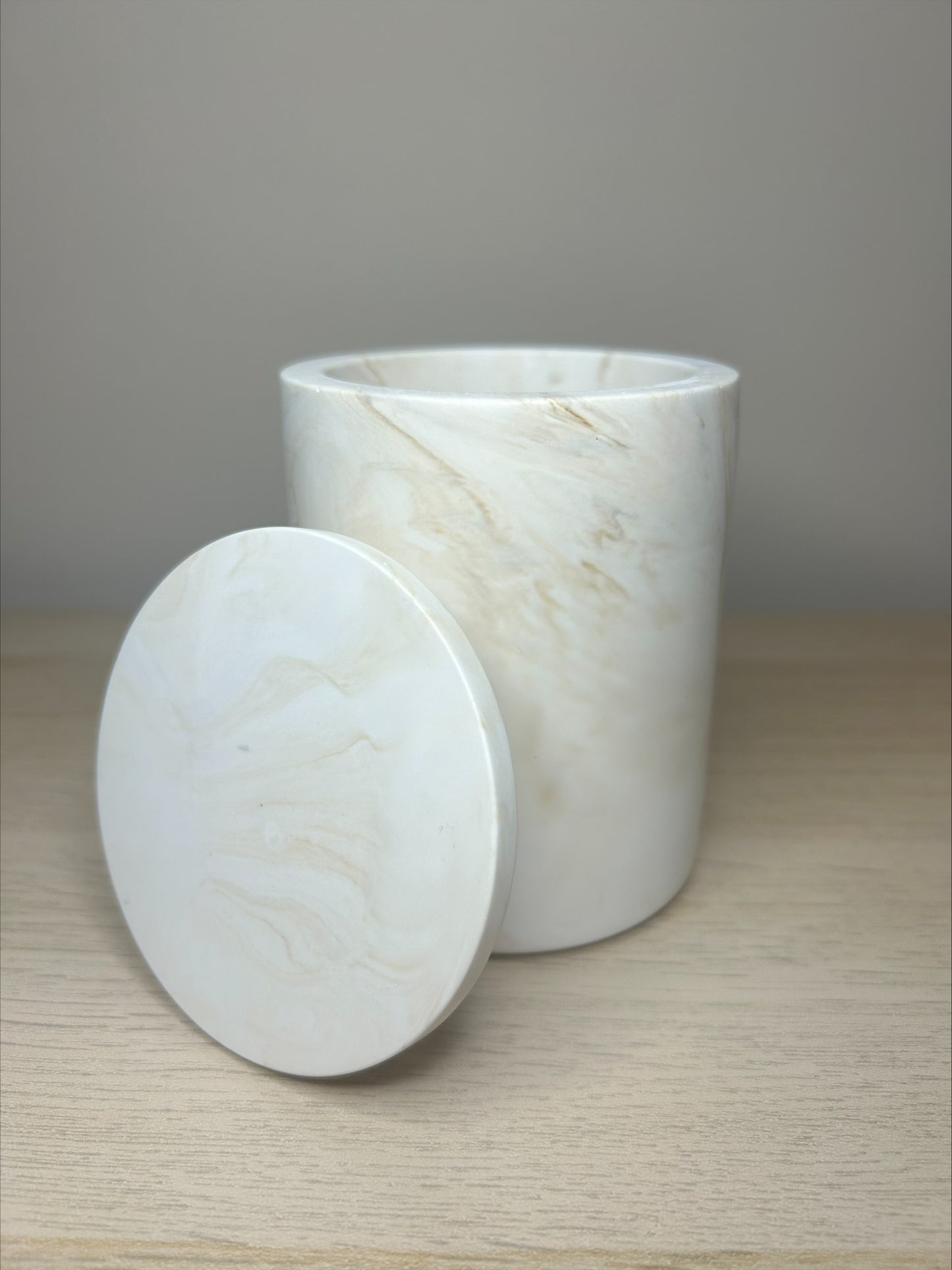 Handmade Home Accessories - a single shot of the beige marble pot with the lid shown slanted against the pot on a wooden surfacec