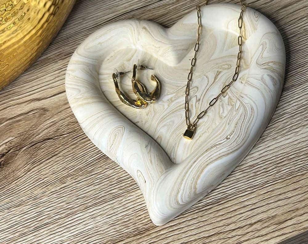 Handmade Home Accessories - A handmade heart shaped chunky trinet dish in a brown marble design on a wooden surface, displaying a pair of gold hoops and a padlock style gold necklace.